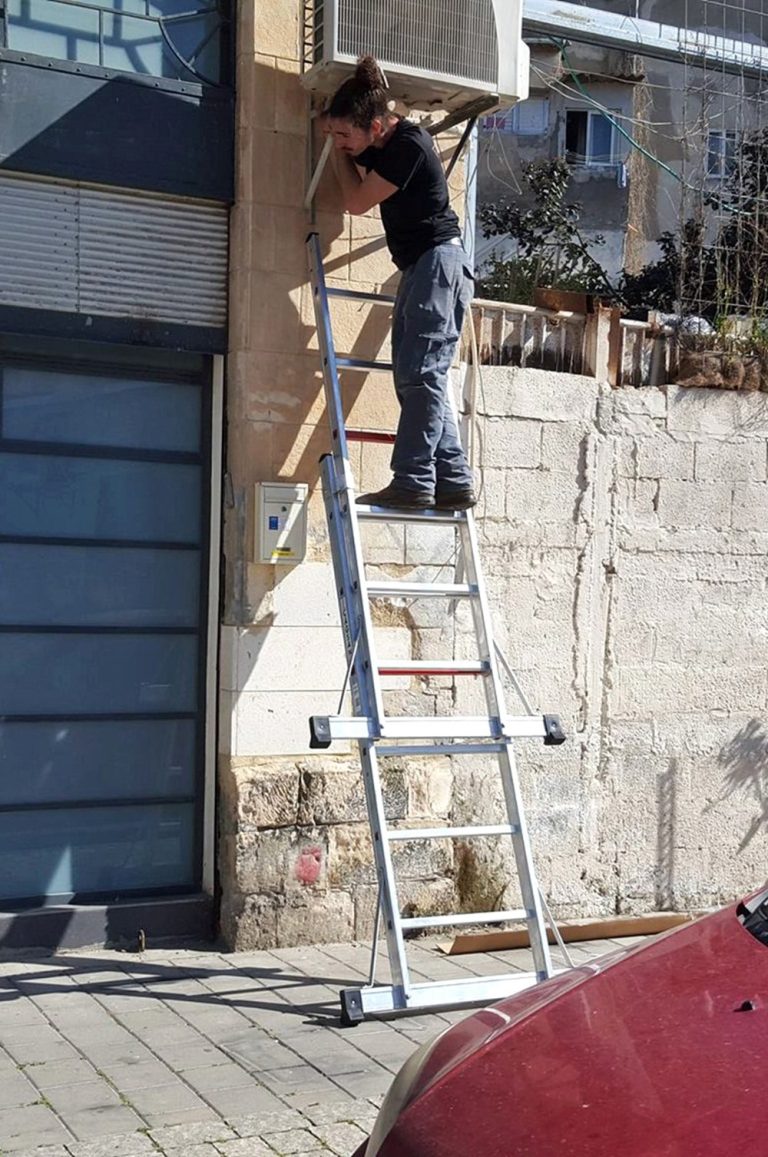 Operario en escalera de andamio Tyrion montando un aire acondicionado